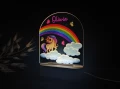 Personalizowana lampka LED dla dzieci z kolorowym motywem tęczy, uroczym jednorożcem stojącym na białych chmurkach i latającymi motylkami, idealna jako dekoracja pokoju dziecięcego oraz wyjątkowy prezent urodzinowy.