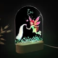 Personalizowana lampka LED dla dzieci przedstawiająca bajkową wróżkę z różdżką, rozsypującą magiczny pył nad roślinną łąką, idealna jako prezent na urodziny i dekoracja pokoju dziewczynki.