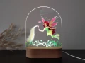 Lampka LED dla dzieci z motywem magicznej wróżki w pastelowych kolorach, unoszącej się nad roślinną łąką, przeznaczona na wyjątkowy prezent urodzinowy lub dekorację pokoju.