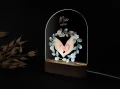 Personalizowana lampka LED z ilustracją dziecięcych stópek i rączek ułożonych w kształt serca, ozdobionych wiankiem z delikatnych zielonych liści i białych kwiatów, idealna na prezent dla noworodka.