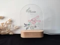 Urocza lampka LED z akrylową szybą z nadrukiem zajączka w pastelowych kolorach, zamontowana na drewnianej podstawie, idealna do pokoju dziecka lub jako personalizowany prezent na chrzest.