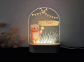 Lampka LED dla dzieci z grafiką uroczego misia na tle zielonej polany i trawy, trzymającego w łapce grzybek, w klimacie natury i lasu.