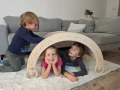 Trójka dzieci bawi się pod bujakiem Montessori 90 cm, wykorzystanym jako tunel.