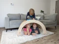 Dzieci siedzą i bawią się na i pod bujakiem Montessori 90 cm w salonie.