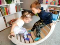 Dwoje dzieci balansuje na bujaku Montessori 90 cm podczas zabawy w pokoju.