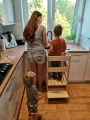 Dwoje dzieci korzysta z kitchen helpera podczas zabawy i obowiązków kuchennych – wieża edukacyjna Montessori w użyciu.