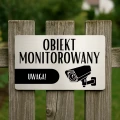 Tablica ostrzegawcza o monitoringu zamontowana na ogrodzeniu.