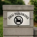 Tablica informacyjna przy budynku firmy z napisem „Zakaz parkowania”.