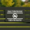Informacyjna tabliczka z zakazem zamocowana na słupku przy drodze.